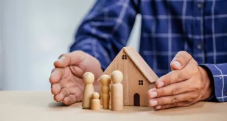 Mains protégeant une maison en bois avec des figurines représentant une famille, symbolisant la SARL de famille immobilière.