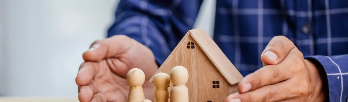 Mains protégeant une maison en bois avec des figurines représentant une famille, symbolisant la SARL de famille immobilière.